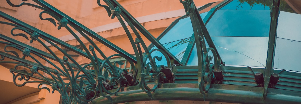 The image displays the entrance to a casino, characterized by detailed and ornate architectural elements with green metal structures and a sign that reads 'CASINO'. The background includes a glass dome and a peach-colored wall.