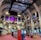 The interior of a large, ornately designed building with arched ceilings and intricate architectural details. The space features gaming machines lined up along the floor, under a high ceiling with a grid pattern. Lighting in purple and white tones enhances the ambiance.